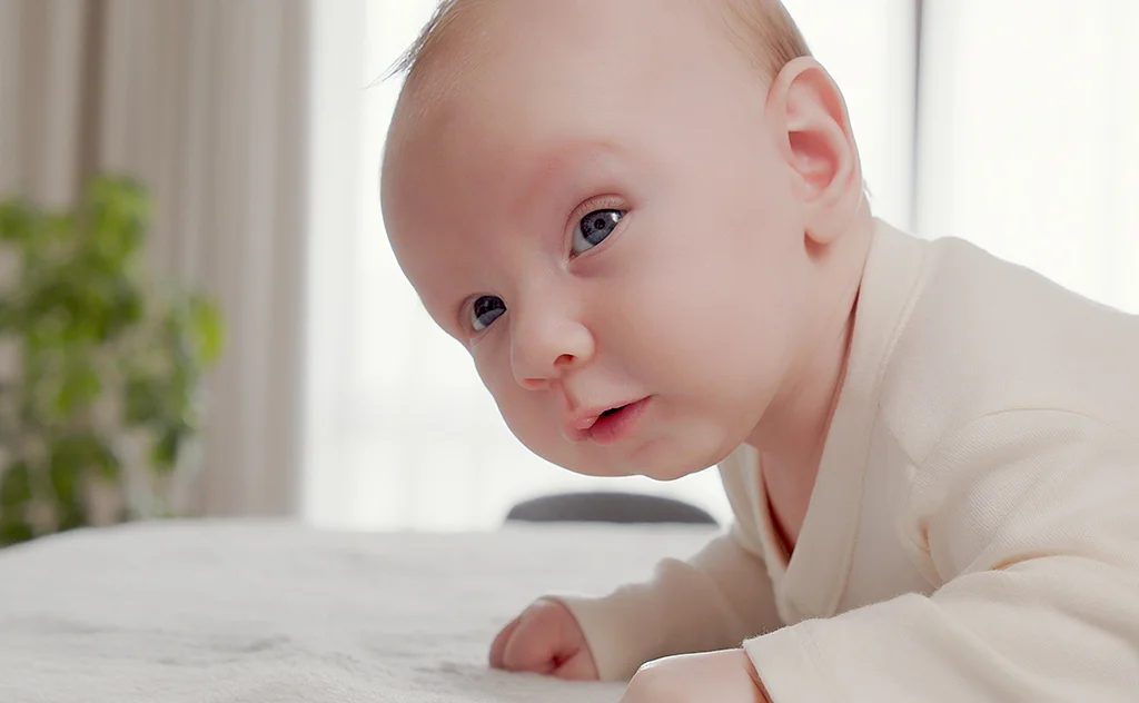 Baby lying on their stomach indoors and looking toward the camera