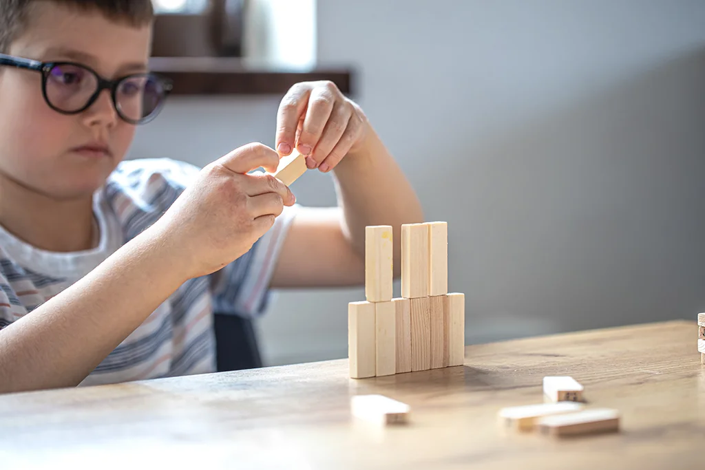 Child wearing glasses building a small tower with wooden blocks on a table