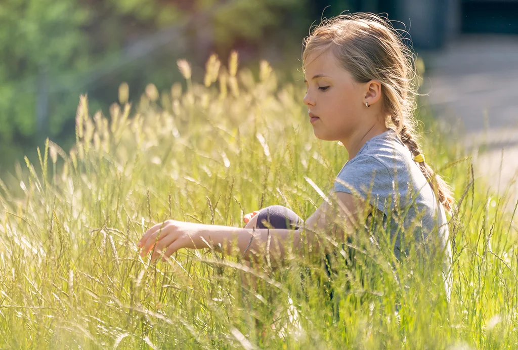 Young child sitting quietly in tall grass outdoors on a sunny day