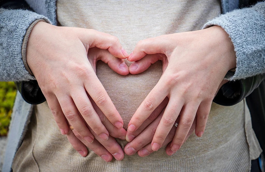 Expecting couple making a heart shape with their hands over a pregnant belly