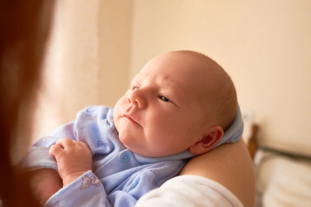 Newborn baby in a blue outfit being gently cradled indoors