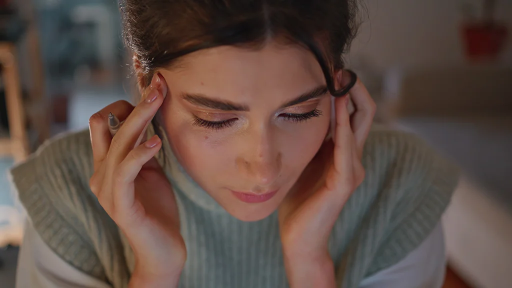 Stressed woman massaging her temples while holding a pen indoors