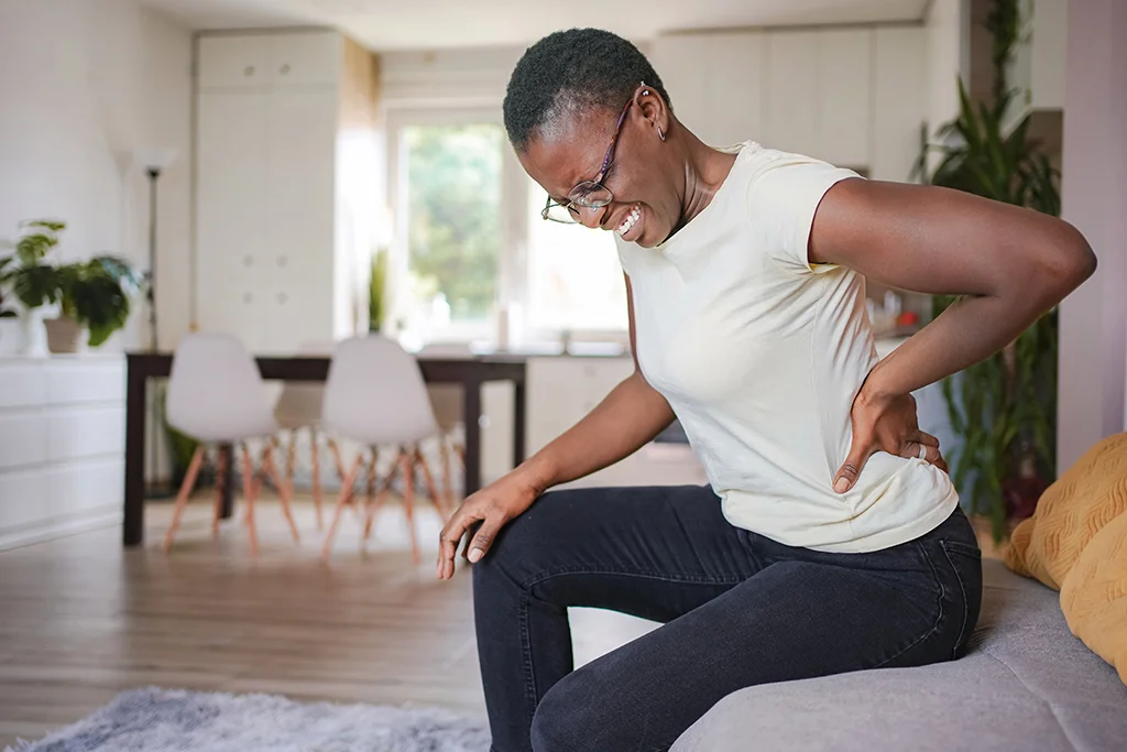 Woman sitting on a couch and holding her lower back in discomfort at home