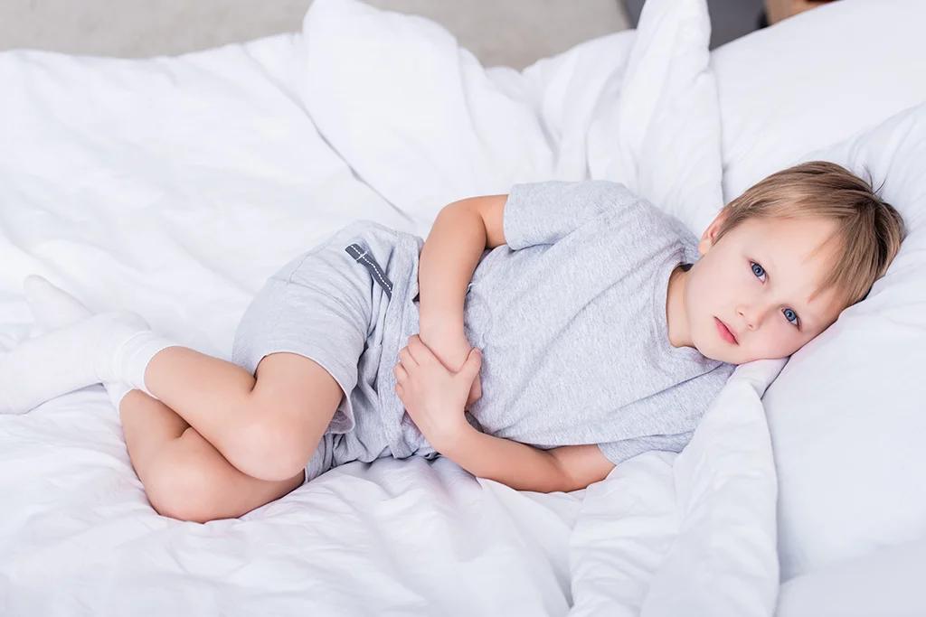 Young boy lying in bed while holding his stomach and looking uncomfortable